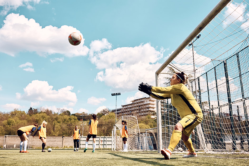 Female goalkeeper catching ball while defending a goal on soccer training at the stadium.